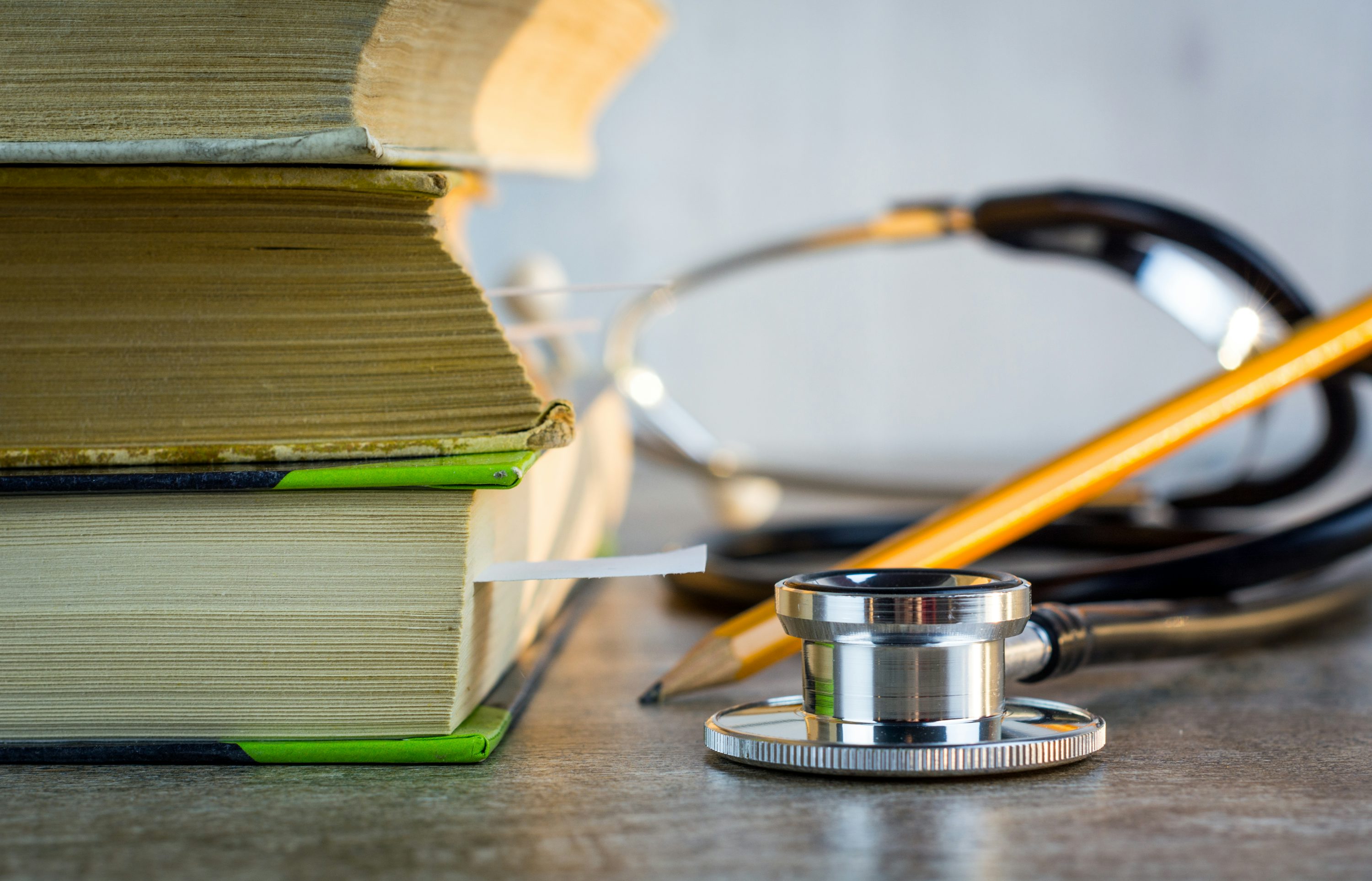 A stethoscope and pencil beside a stack of textbooks.