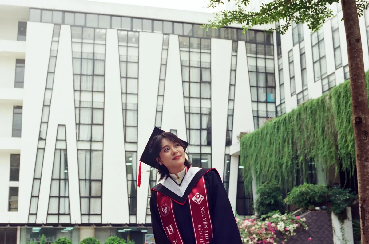 身着学位服的年轻女性在户外现代建筑旁微笑留影。